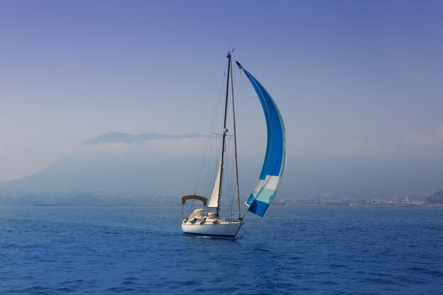 Mar azul con velero navegando en una costa de niebla.