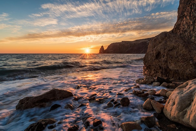 Mar brillante atardecer las olas chocan contra la roca iluminada por la cálida puesta de sol arena y guijarros volcánicos