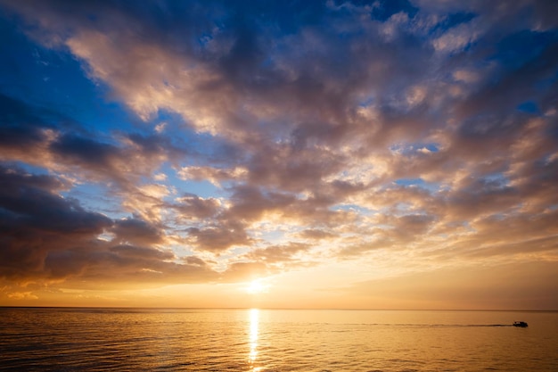 Mar en calma con cielo al atardecer y sol a través de las nubes sobre