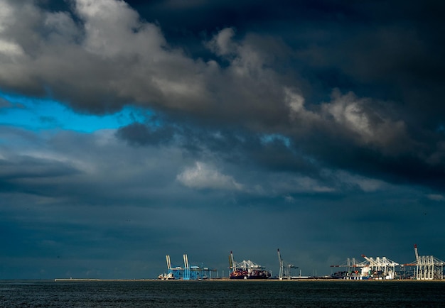 Mar calmo com guindastes à distância contra o céu