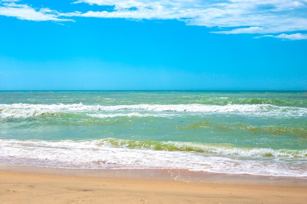 Mar com ondas e céu azul da costa arenosa no horizonte Viagens e turismo