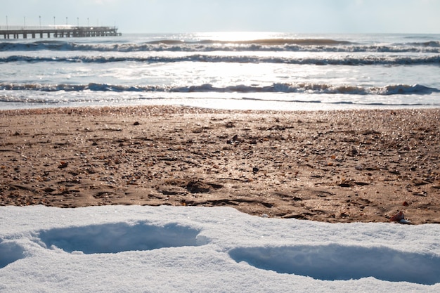 Mar frío con un muelle y nieve en la orilla arenosa Mar Negro en invierno