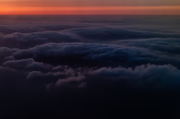 Mar incrível de nuvens fofas escuras ao pôr do sol, visto do avião, horizonte laranja.