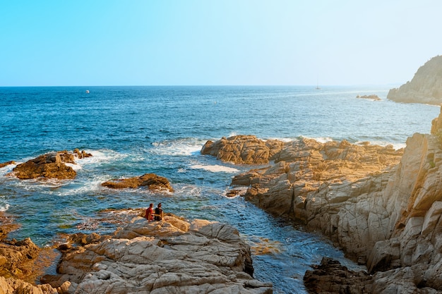 Mar. jovem casal em uma costa rochosa no sunse