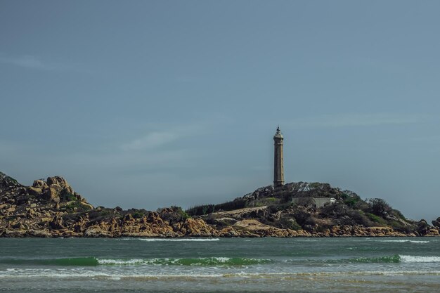 Mar naturaleza vista panorámica paisaje fondo Océano acantilados rocosos isla boscosa Cielo azul claro Faro en la cima de la montaña Señal advierte a los marineros naufragio concepto de viaje esperanza propósito de la vida