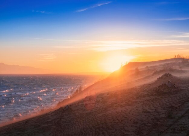 Foto mar ou lago contra o pano de fundo de montanhas com grandes dunas de areia durante o pôr do sol paisagem