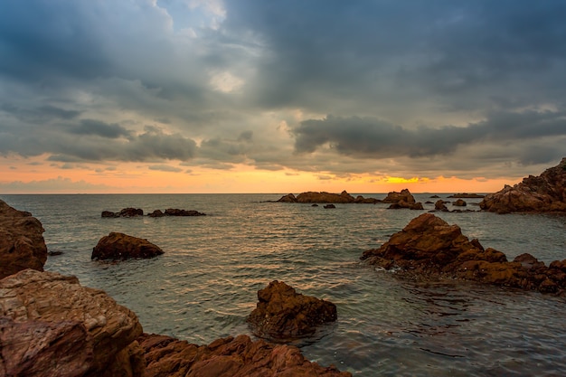 El mar y las rocas y el cielo tormentoso atardecer nublado sobre el mar en una playa rocosa con piedras