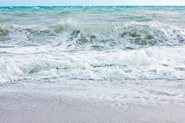 Mar tormentoso e céu azul, espuma do mar branco em uma praia arenosa amarela.