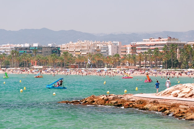 Mar transparente e turquesa, praia com turistas em Salou, Espanha.
