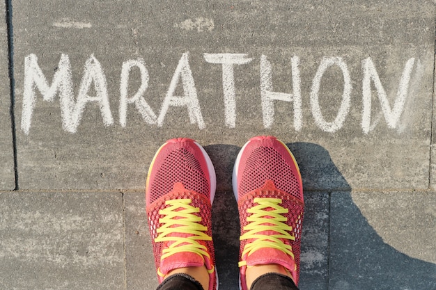 Marathon geschrieben auf grauen Bürgersteig mit den Frauenbeinen in Turnschuhe