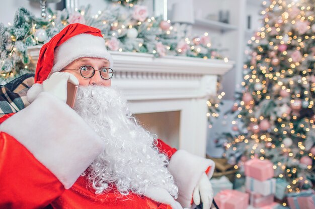 Maravilha Papai Noel senta-se na sala festiva, falando no telefone.