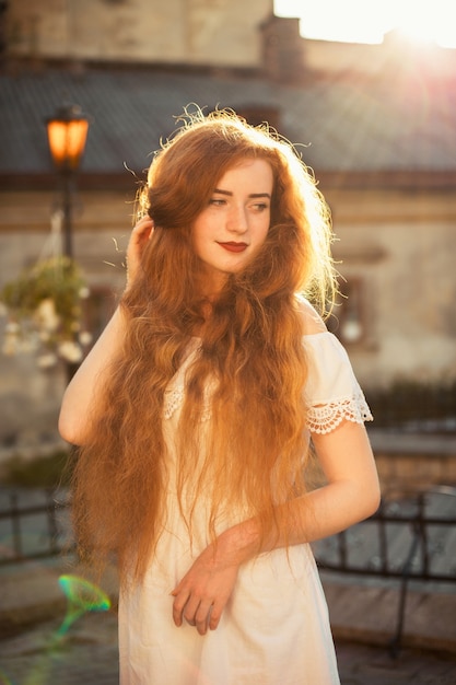 Maravilhosa jovem ruiva com cabelo comprido e ondulado nu posando no brilho do sol ao pôr do sol