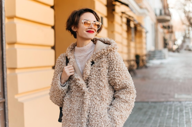 Maravilhosa mulher de cabelos curtos andando pela cidade em dia frio tiro ao ar livre de modelo feminino positivo no casaco