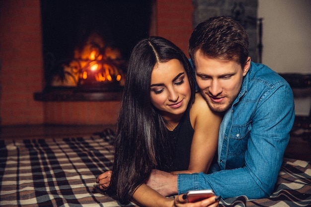 Maravillosa foto de jóvenes enamorados. La abraza. Mantienen los ojos cerrados. Pareja acostada no lejos de la chimenea