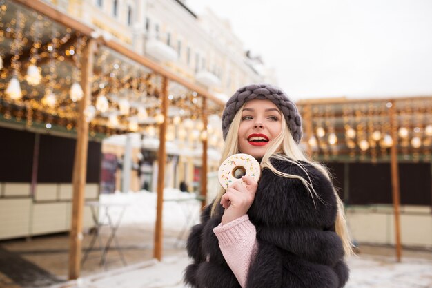 Maravillosa modelo rubia sosteniendo una deliciosa galleta de jengibre contra una decoración ligera en la feria de Navidad en Kiev