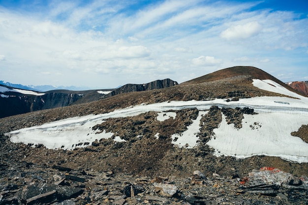 Maravillosa vista al pequeño glaciar en una colina pedregosa bajo un cielo azul con nubes.