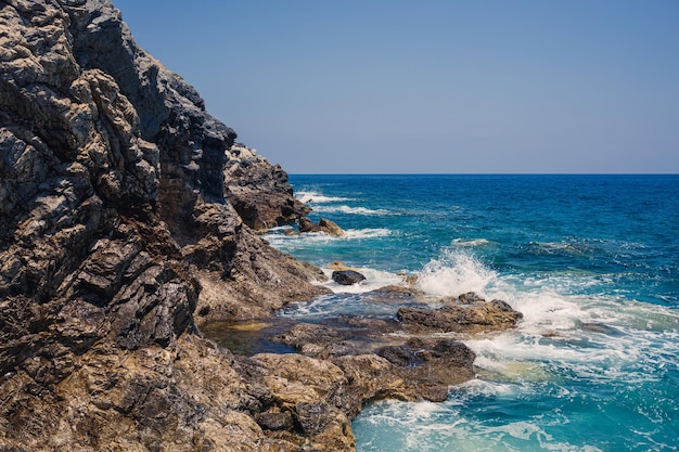 Maravillosas vistas del mar Mediterráneo azul Rocas soleadas olas con espuma y agua salpicada La ola choca contra las rocas en la orilla