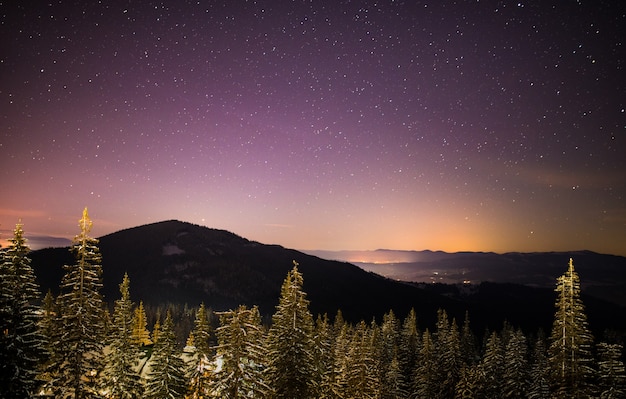 El maravilloso cielo estrellado se encuentra sobre las pintorescas vistas de la estación de esquí entre las montañas de colinas y árboles.