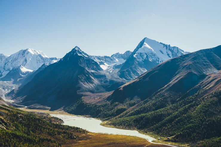 Foto maravilloso paisaje alpino con lago de montaña y río de montaña en el valle con bosque en colores otoñales sobre fondo de siluetas de montañas nevadas bajo un cielo azul. hermoso valle de montaña en otoño