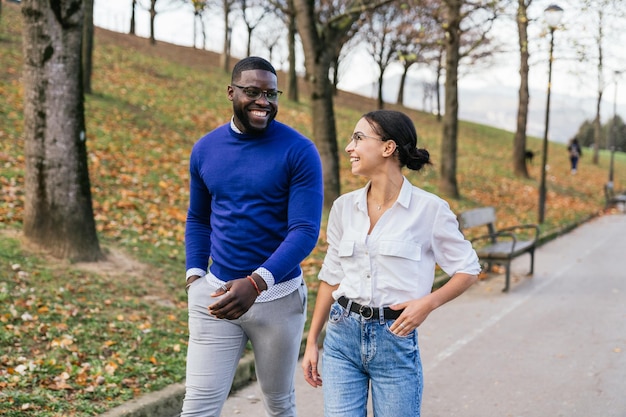 Maravilloso paseo otoñal Feliz niño negro y niña caucásica hablando y paseando en un parque en medio de las hojas que caen