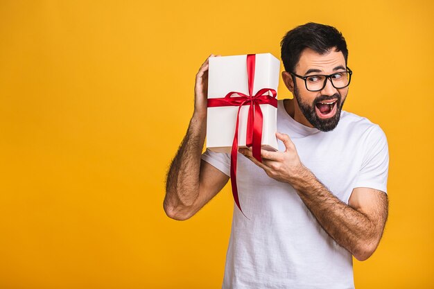 ¡Maravilloso regalo! Adorable foto de atractivo hombre barbudo con hermosa sonrisa con caja de regalo de cumpleaños aislada sobre fondo amarillo.