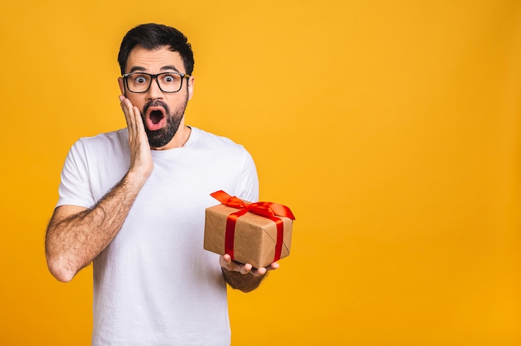 Foto ¡maravilloso regalo! adorable foto de atractivo hombre barbudo con hermosa sonrisa con caja de regalo de cumpleaños aislada sobre fondo amarillo.