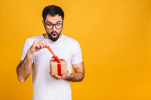 ¡Maravilloso regalo! Adorable foto de atractivo hombre barbudo con hermosa sonrisa con caja de regalo de cumpleaños aislada sobre fondo amarillo.