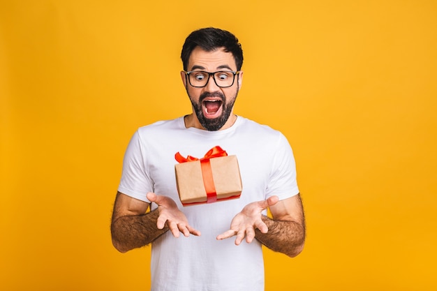 ¡Maravilloso regalo! Adorable foto de atractivo hombre barbudo con hermosa sonrisa con caja de regalo de cumpleaños aislada sobre fondo amarillo.