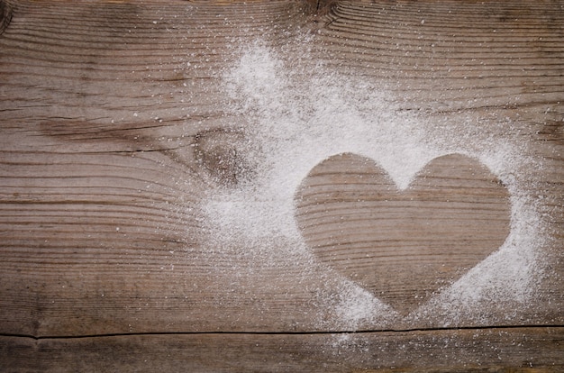 Marca en forma de corazón con azúcar en polvo sobre mesa de madera