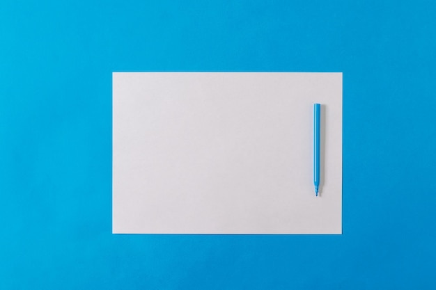 Marcador azul en una hoja de papel blanca sobre un fondo azul Minimalismo Tendencia de color del lugar de trabajo