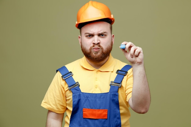 Marcador de tenencia estricta joven constructor hombre en uniforme aislado sobre fondo verde