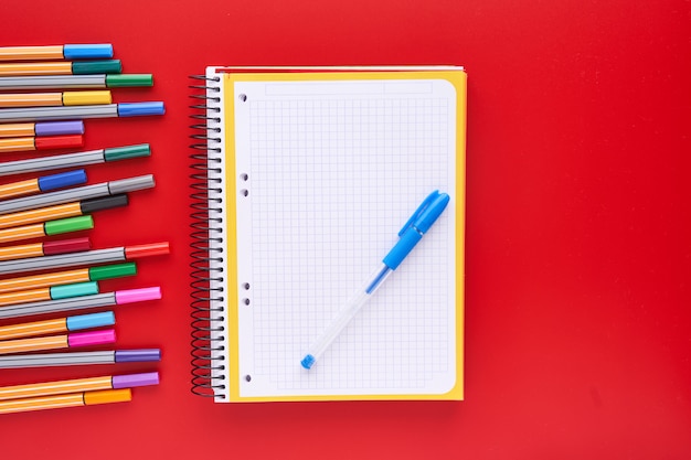 Marcadores coloridos e um caderno sobre um fundo vermelho. Voltar ao conceito de escola e artesanato.