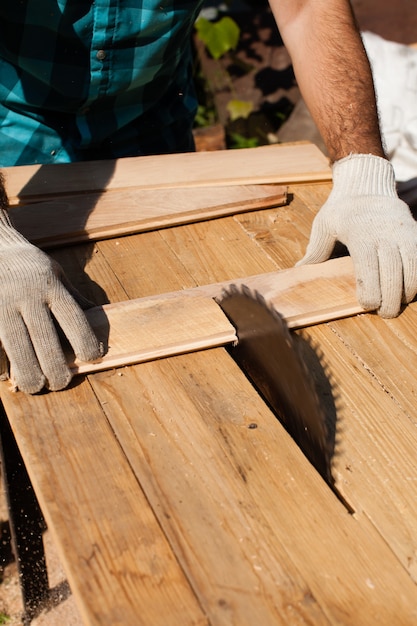 Marceneiro que trabalha duro cortando prancha de madeira, foco na serra