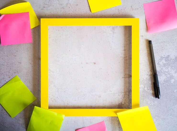 Foto marco amarillo vacío y pegatinas de papel para notas y bolígrafo sobre fondo de hormigón gris