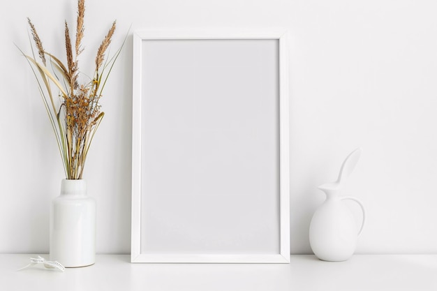 un marco blanco con un jarrón blanco y flores secas