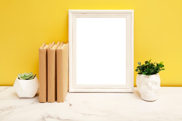 Marco blanco vacío con una casa plantas y libros sobre la mesa sobre fondo amarillo