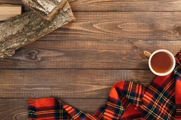 Marco de bufanda roja femenina de moda, taza de té, leña sobre fondo de madera