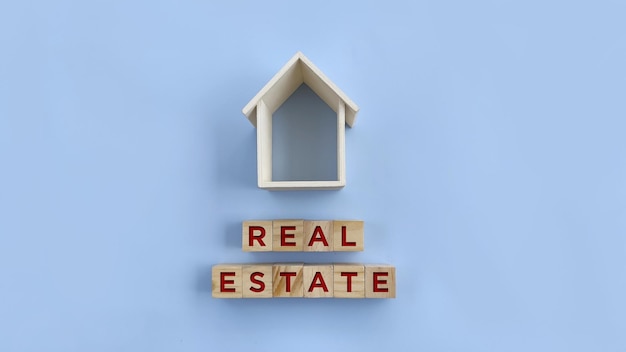 Marco de casa de madera con palabra inmobiliaria en bloque de madera sobre fondo azul Símbolo inmobiliario