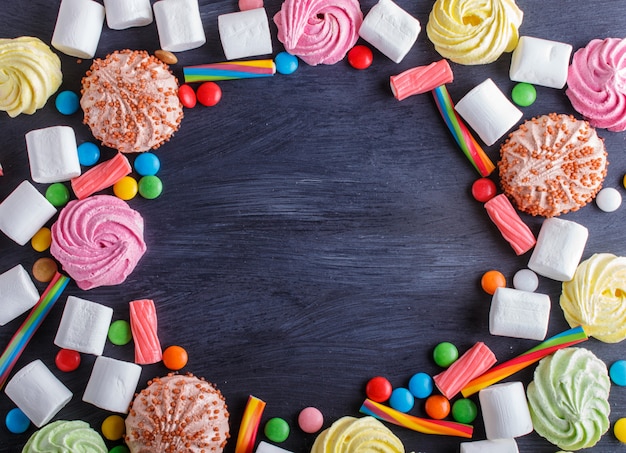 Marco colorido de caramelos multicolores en fondo de madera negro.
