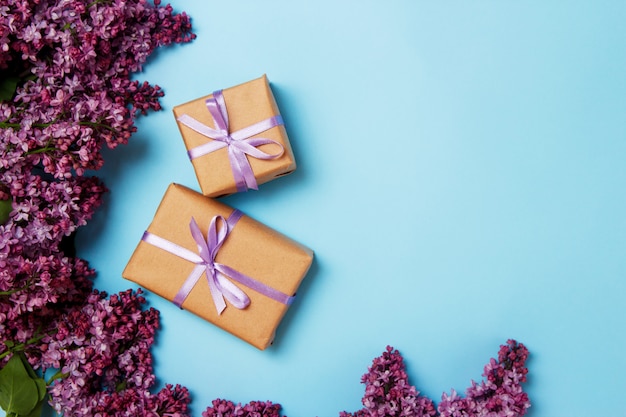 Marco de flores lilas con dos cajas de regalo sobre un fondo azul