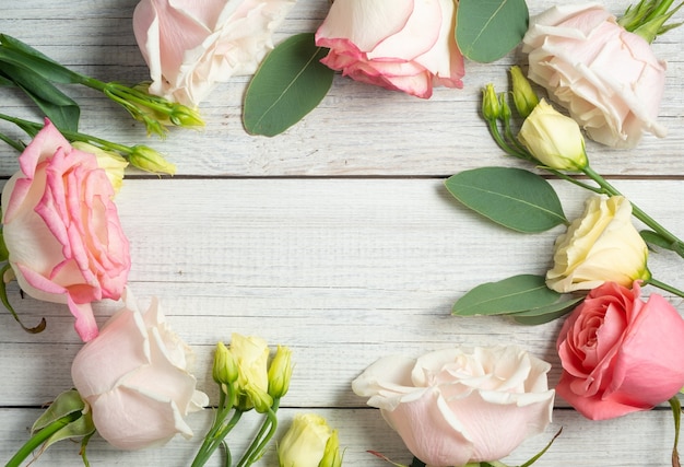 Marco de flores sobre un fondo cutre de madera blanca. Eustoma cremoso, eucalipto y rosas rosadas.