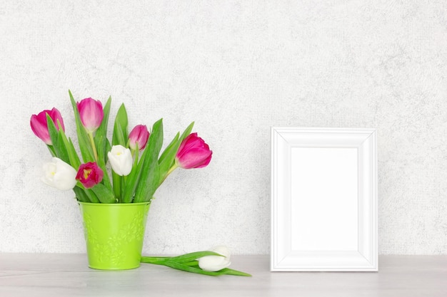Foto marco de fotos blanco en blanco con ramo de flores de tulipán en la mesa fondo de maqueta de primavera