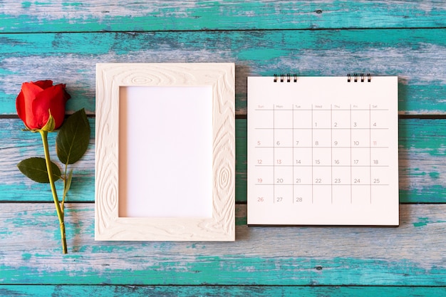 Foto marco de fotos en blanco, calendario y rosas rojas sobre mesa de madera