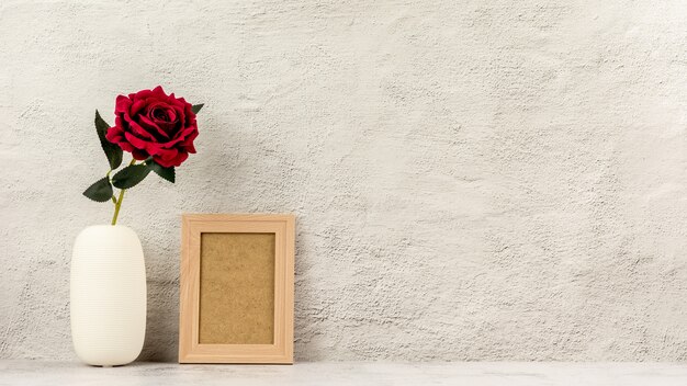 Marco de fotos clásico de madera y una rosa roja en florero.