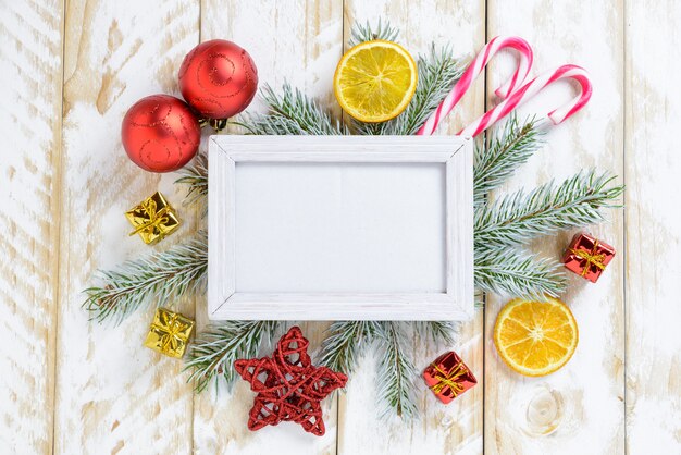 Marco de fotos entre la decoración de Navidad, con bastones de caramelo y cajas de regalo en una mesa de madera blanca. Vista superior, marco para copiar espacio