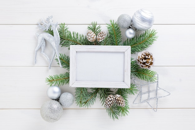 Marco de fotos con decoración de Navidad, con bolas blancas y piñas en una mesa de madera blanca. Vista superior, marco para copiar espacio