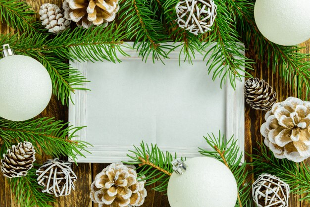 Marco de fotos entre la decoración de navidad, con bolas blancas y piñas en una mesa de madera marrón. vista superior, marco para copiar espacio.