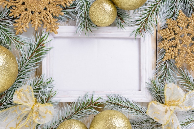 Marco de fotos entre la decoración de Navidad, con bolas de color dorado y copos de nieve sobre una mesa de madera blanca. Vista superior, marco para copiar espacio