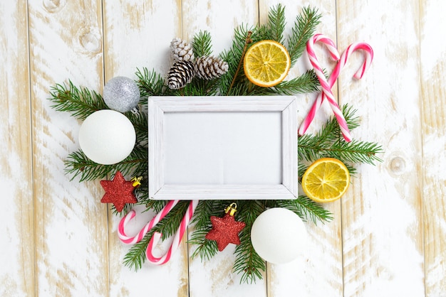 Marco de fotos entre la decoración de Navidad, con bolas de colores y bastón de caramelo sobre una mesa de madera blanca. Vista superior, marco para copiar espacio.