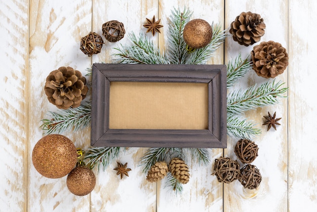 Marco de fotos entre la decoración de Navidad, con bolas marrones y piñas en una mesa de madera blanca. Vista superior, marco para copiar espacio